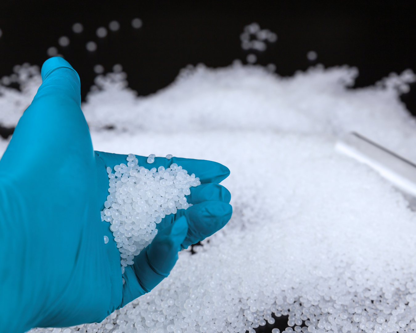 Hand in blue glove holding recycled plastic pellets over a pile of plastic granules