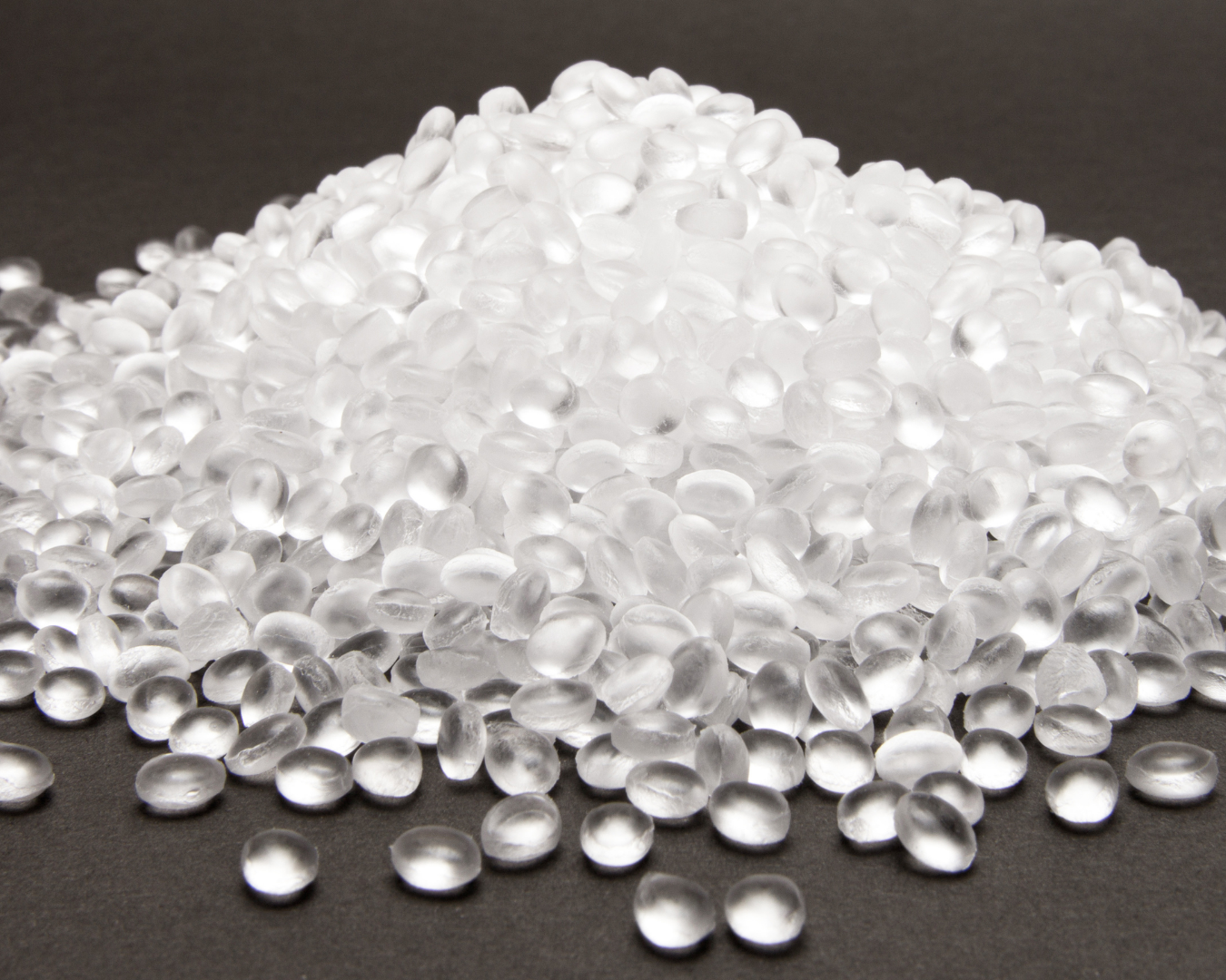 Close-up of transparent plastic pellets piled on a dark surface